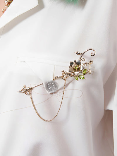 Close up of Tighnari jewelry showing metal flower pendant and green gem details